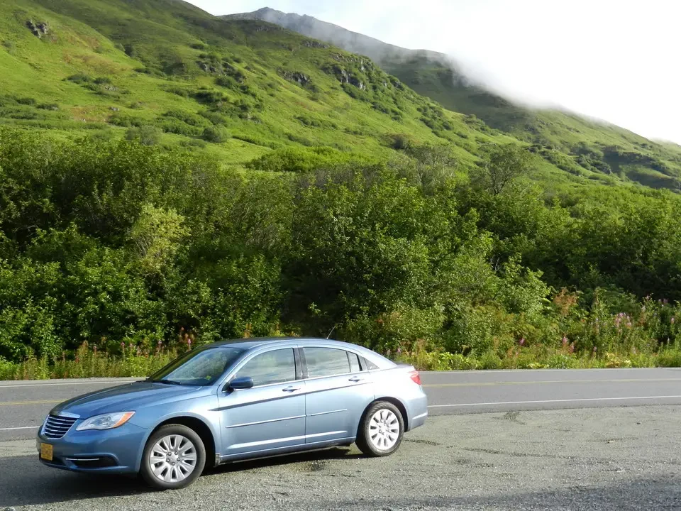 Un'automobile blu si muove su una strada panoramica attraverso colline verdi.