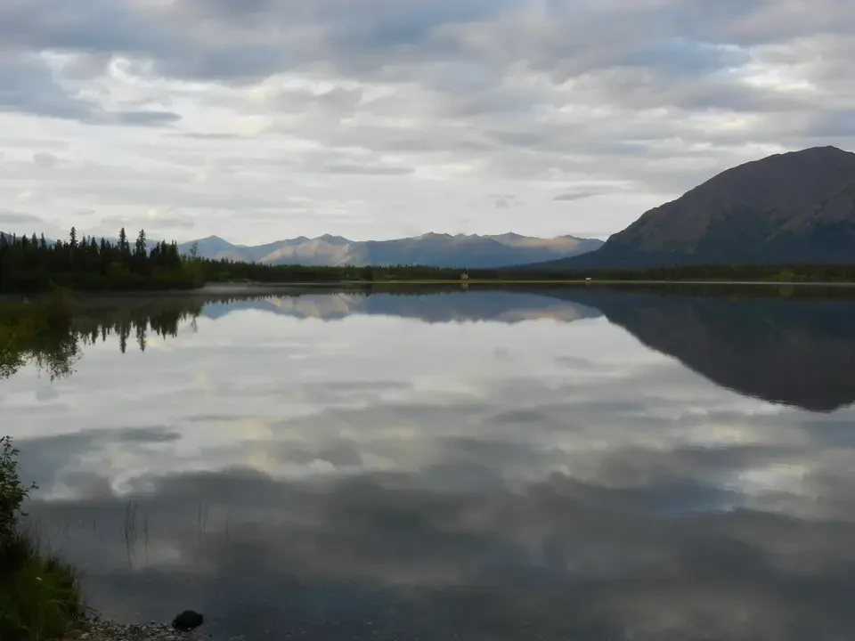 A body of water reflects mountains and clouds in a serene landscape.