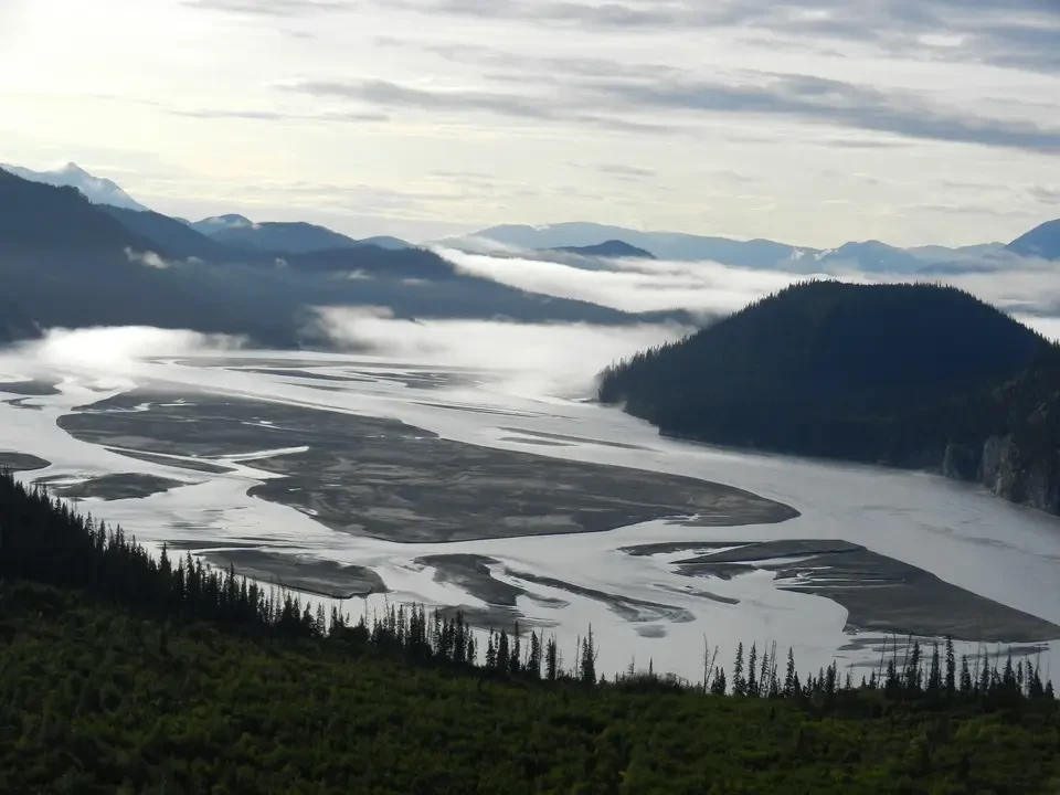 A river flows through a mountain valley covered in morning fog.