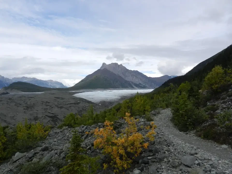 A mountain landscape with glaciers and snow-capped forests under a cloudy sky.