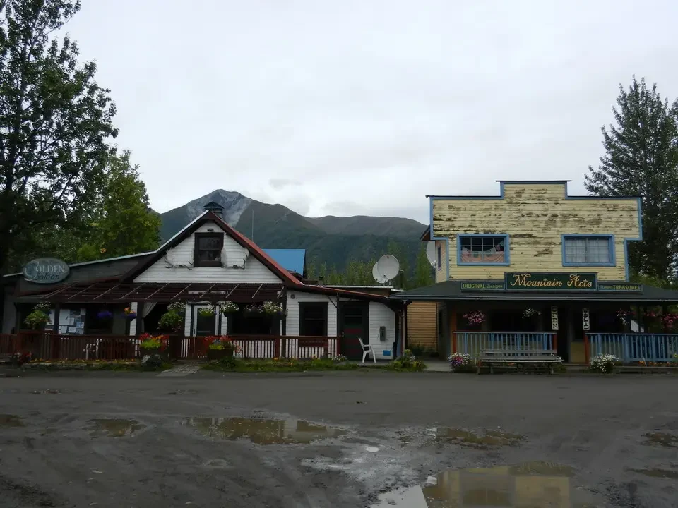 A rustic building with a sloping roof stands in front of snow-capped mountains.