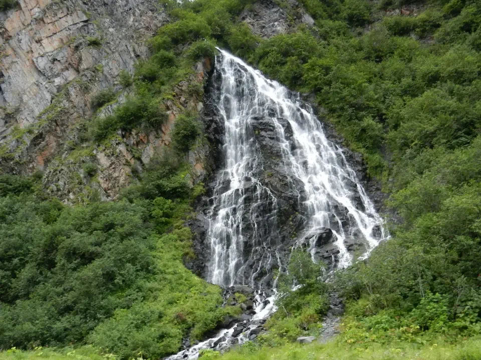 A waterfall flows vigorously between rocks and lush vegetation.