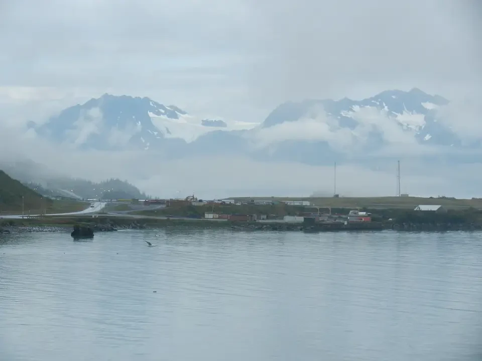 Fog-shrouded snow-capped mountains loom above a coastline.