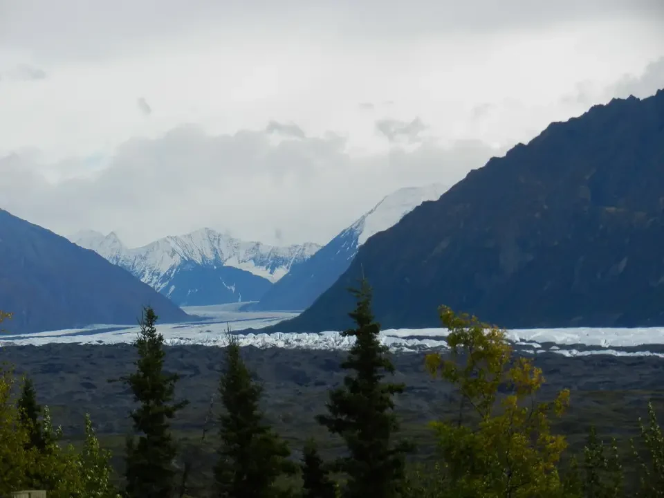 A vast mountain landscape with glaciers and snow-capped mountains under an overcast sky.