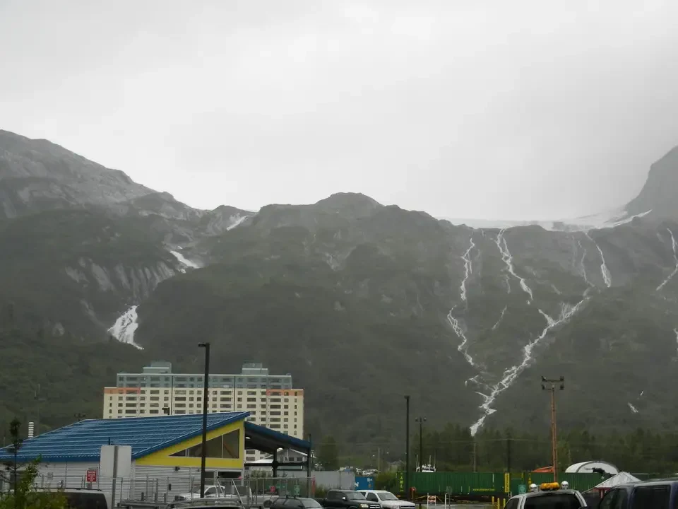 A tower rises between snow-capped mountains under an overcast sky.