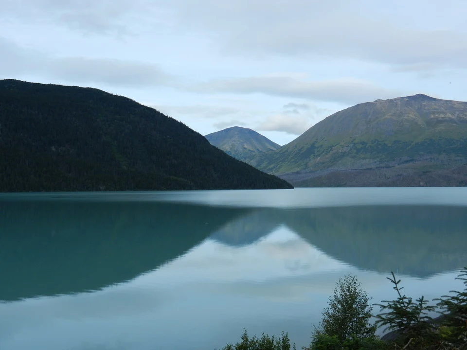 An alpine lake with forested mountains and reflections on the calm water.