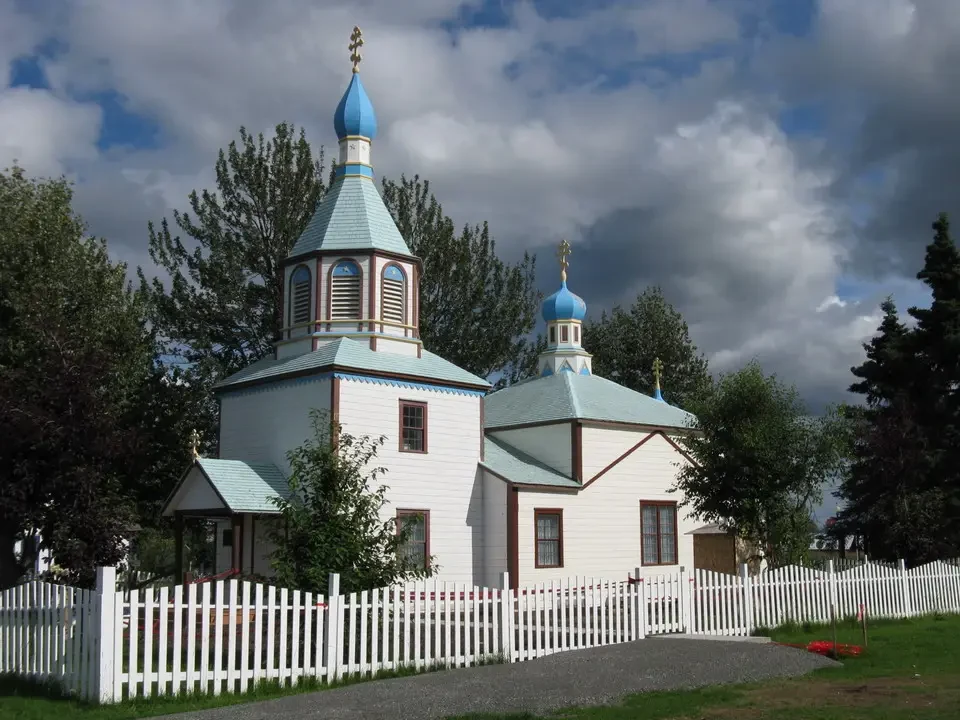 A white Orthodox church with blue roofs stands in an outdoor setting.