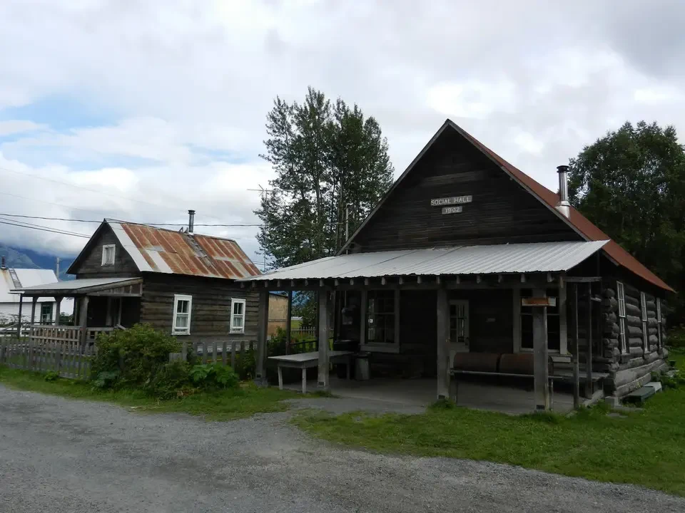 An old wooden structure with a pitched roof sits in a rural setting.