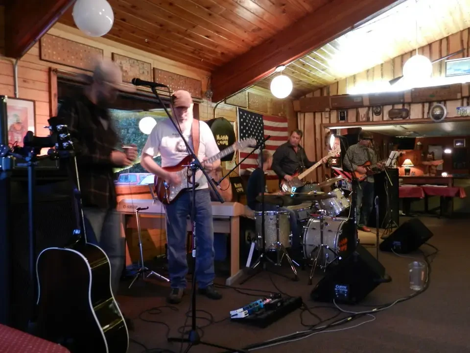 A musical group plays in a rustic interior setting.