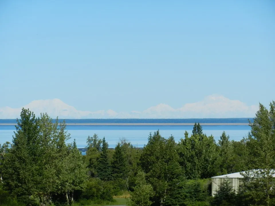 A landscape shows a lake with mountains in the background under a blue sky.