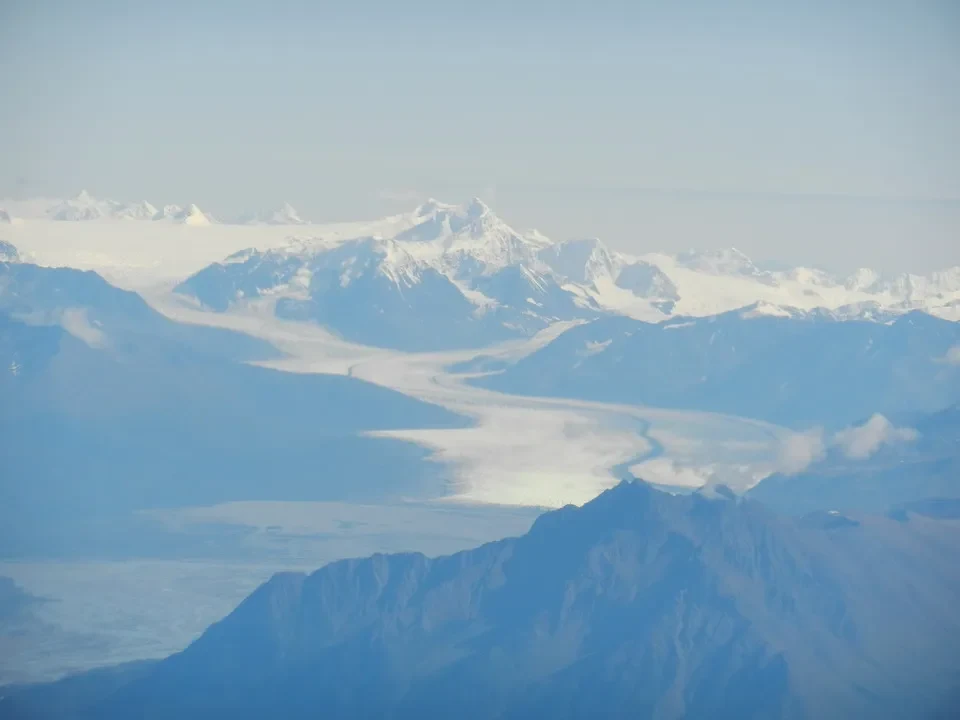 Snow-capped mountain ranges stretch beneath a bright sky.