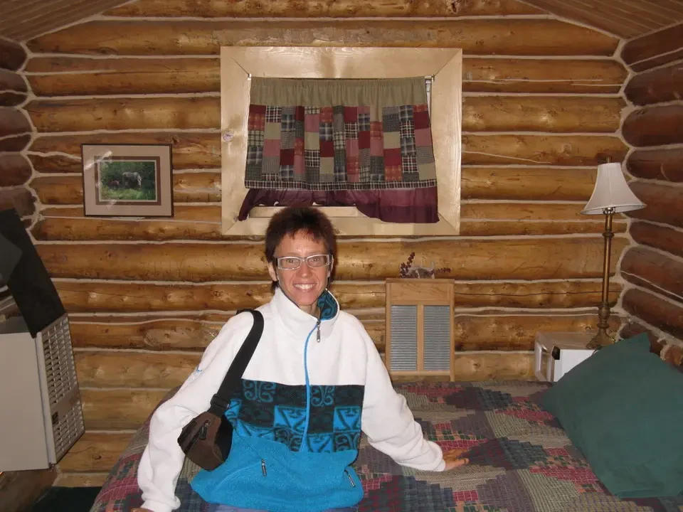 A man smiles in a rustic log cabin with a fireplace.