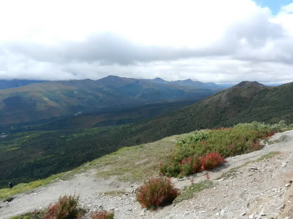 A mountain panorama with green forests and distant peaks under a cloudy sky.