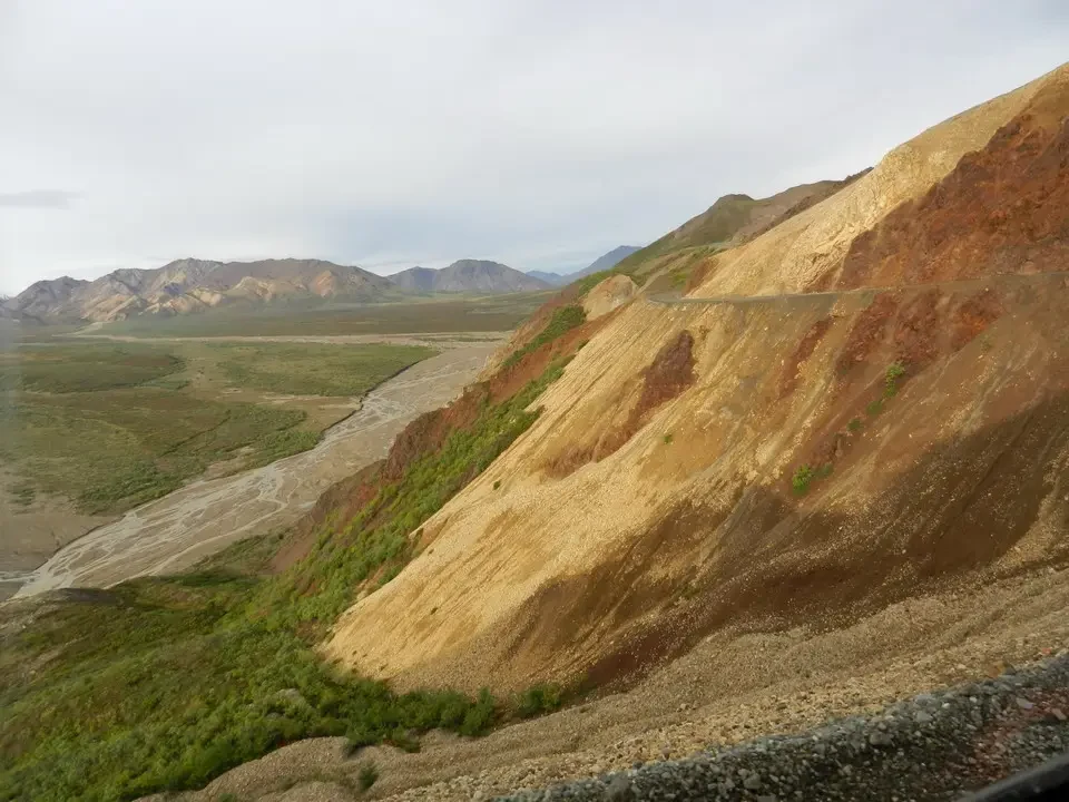 A canyon landscape with colorful rocky slopes under a cloudy sky.