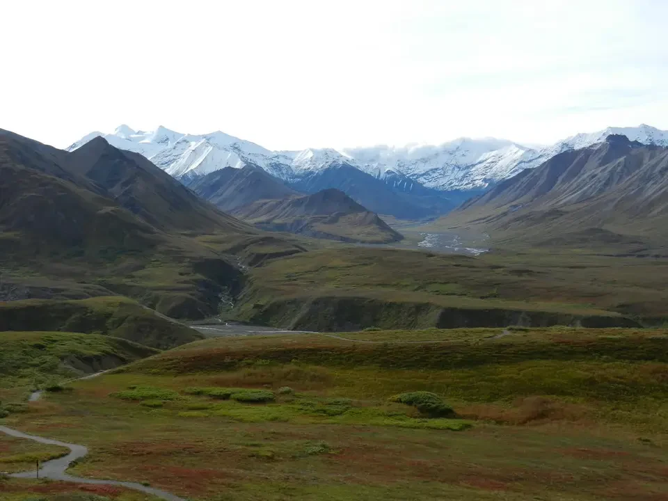 A vast mountain landscape with snow-capped peaks and grassy slopes.