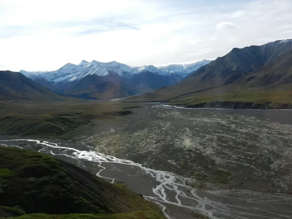 A river flows through a mountain landscape with snow-capped mountains in the background.