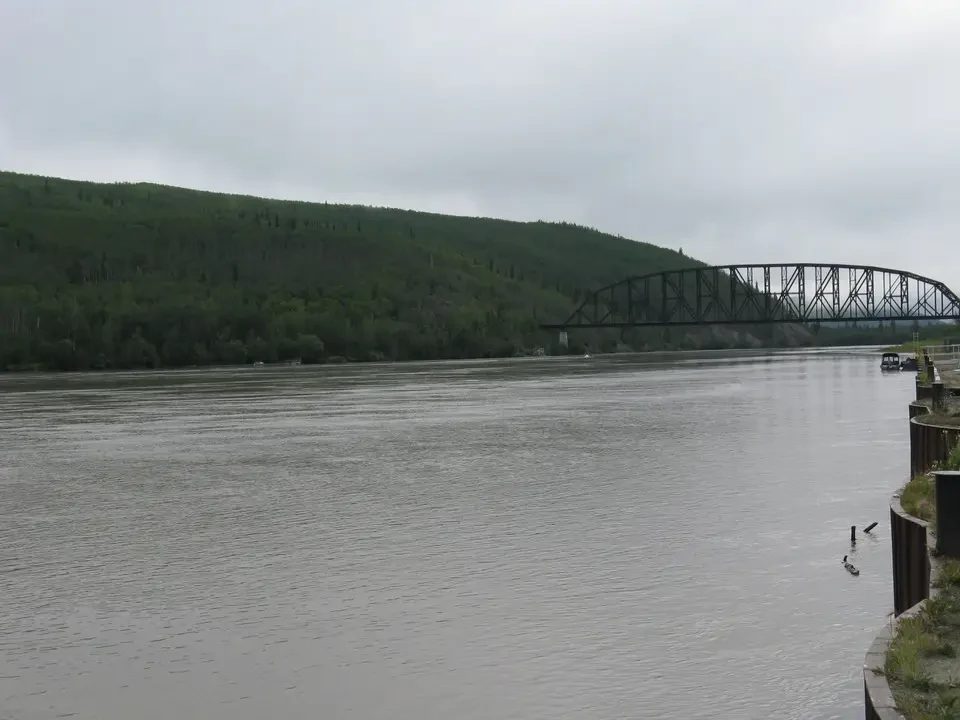 A railway bridge crosses a river with forested hills in the background.