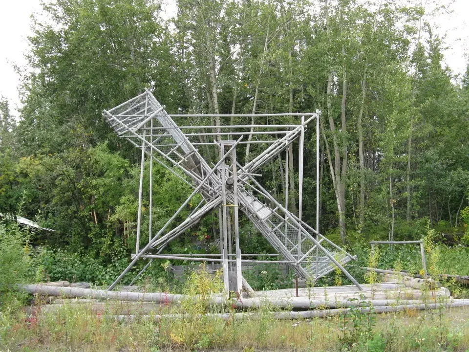 A wheel-shaped metal structure is visible outdoors among trees.