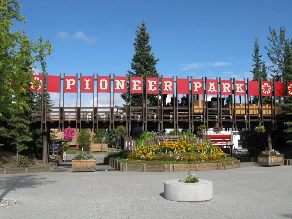 A park with a red fence and green vegetation stretches under a blue sky.