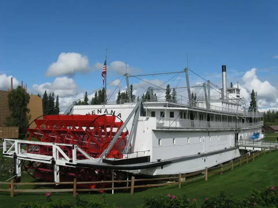 A white historic ship with red details is displayed on a green lawn.