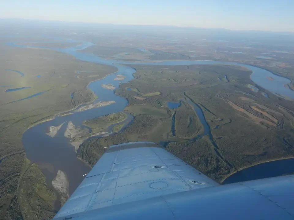 A meandering river flows through a flat, forested landscape in Alaska.