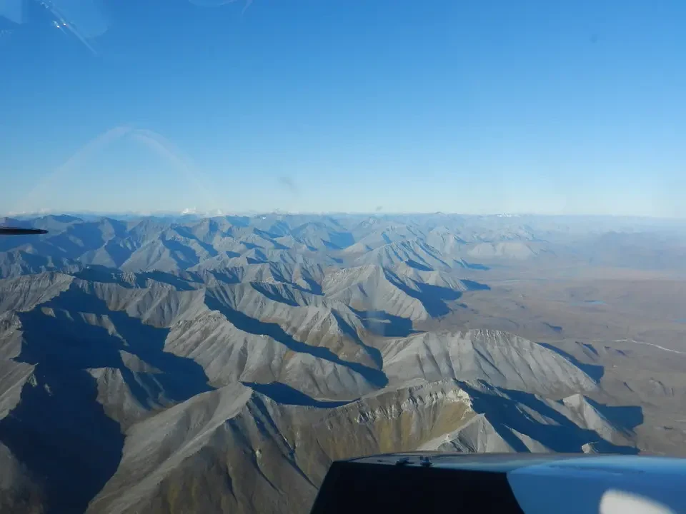 Mountain landscape with jagged peaks and long shadows under a blue sky.