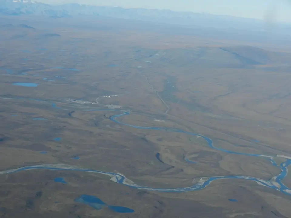 A meandering river flows through a vast, arid plain with rolling terrain.