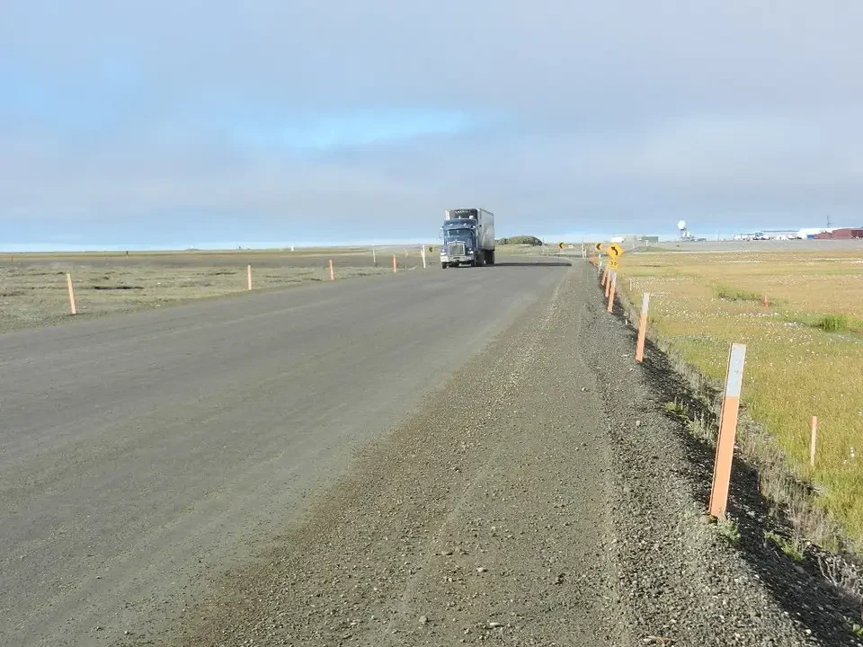 A truck travels on a dirt road in an open landscape.