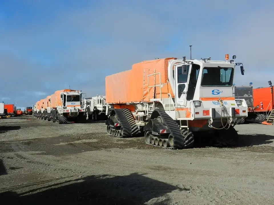 Trucks with trailers are parked on a dirt lot.