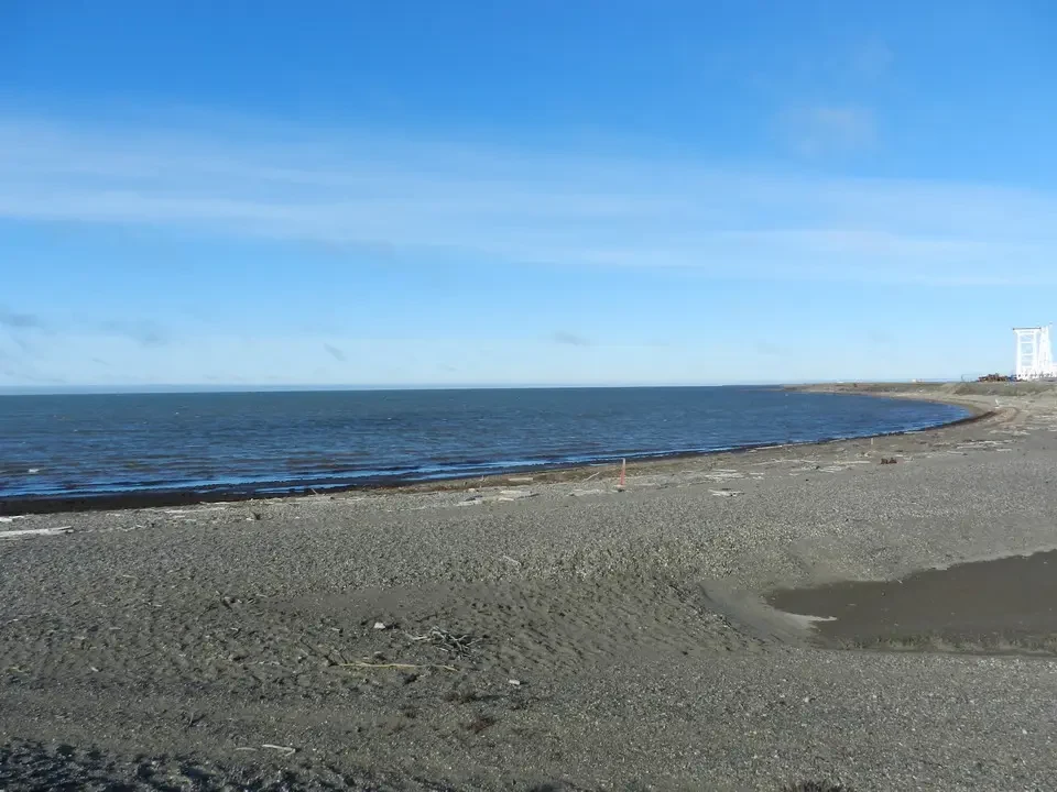 A rocky beach stretches along the coast under a blue sky.