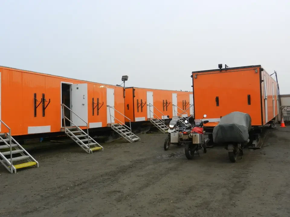 Orange wagons with stairs are parked on a dirt lot.