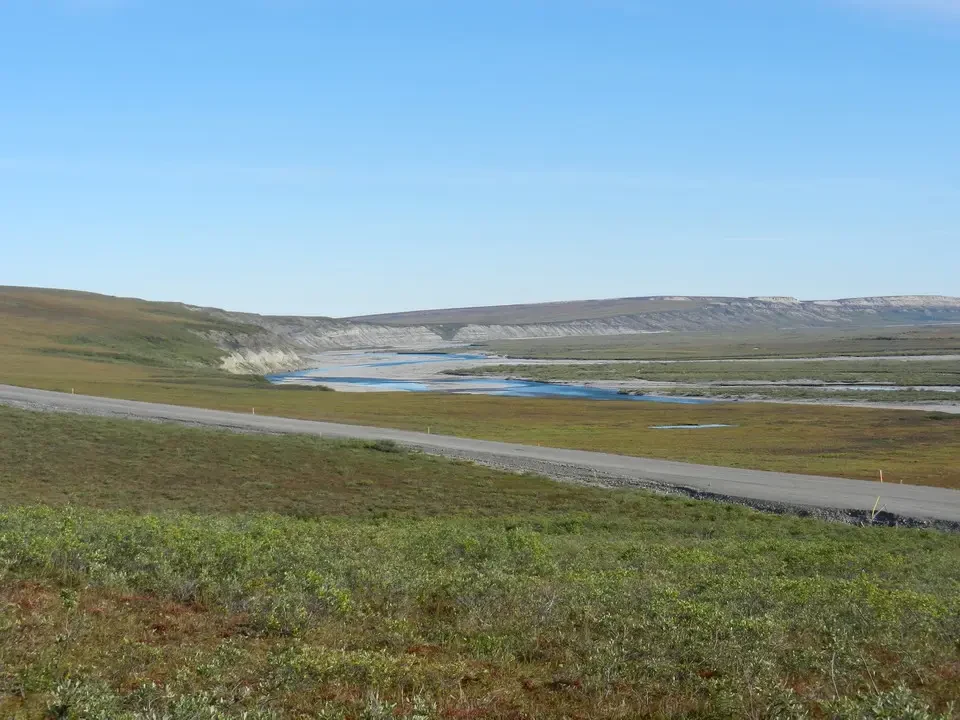 A sweeping panorama shows a river flowing across a vast grassy plain under a blue sky.