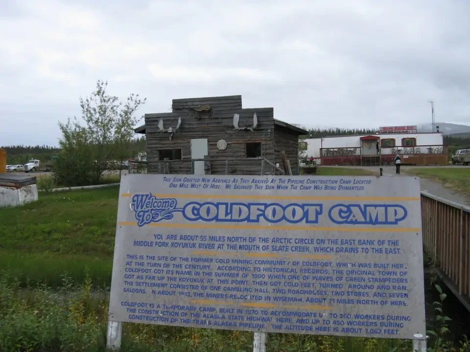 A wooden building with a sign on the street shows a rural scene.