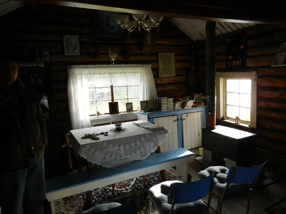 A standing man looks through a bright window in a rustic interior.