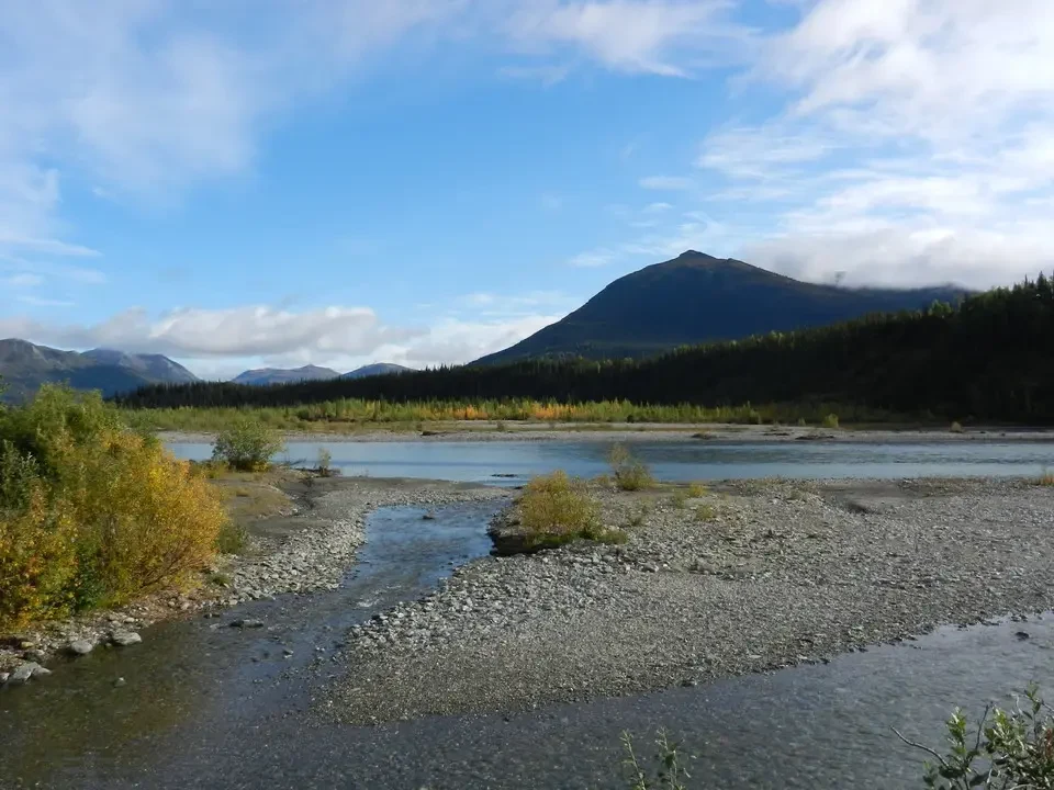 A river flows through a mountain landscape with a towering mountain in the background.