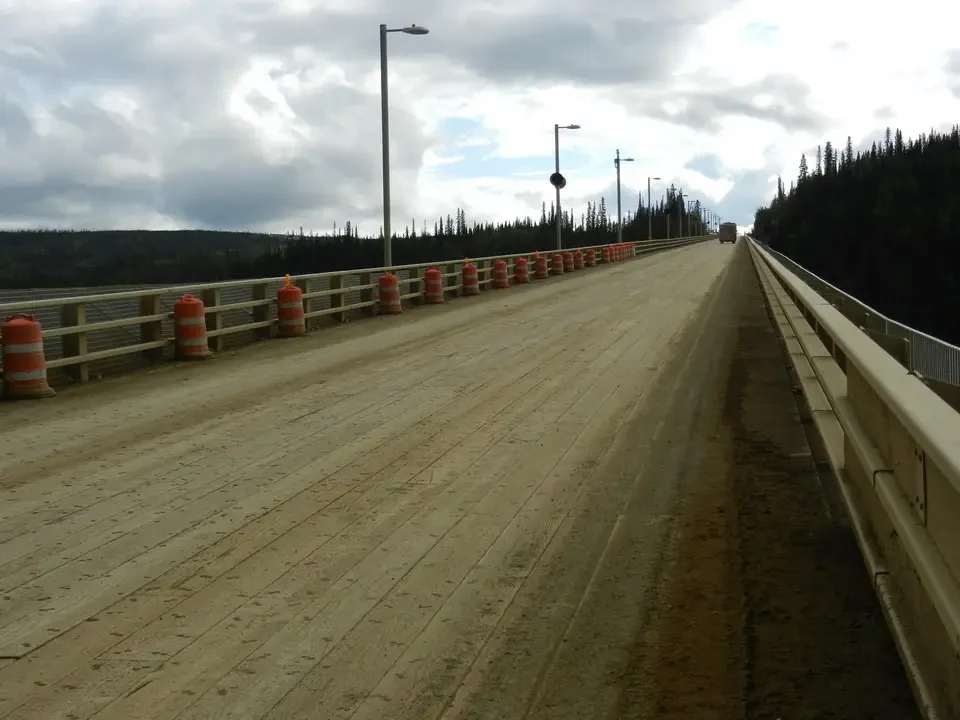 An asphalt road stretches through a forested landscape under a cloudy sky.