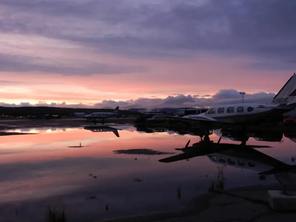 Planes are reflected on water during sunset at an airport.