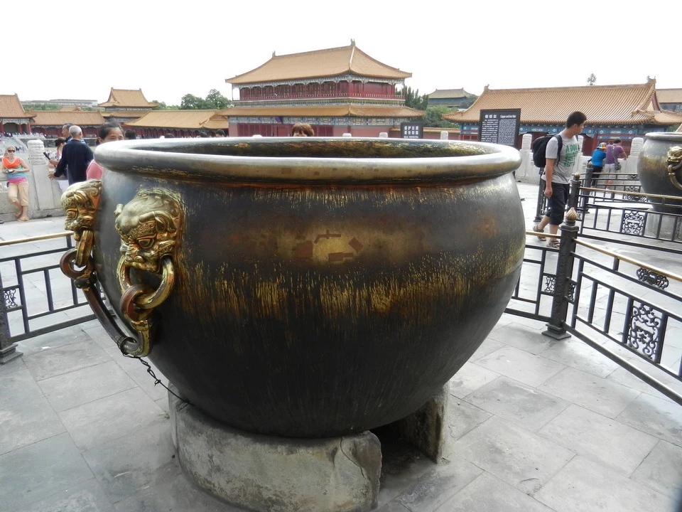Una grande vasca in bronzo si trova davanti a un edificio tradizionale cinese.