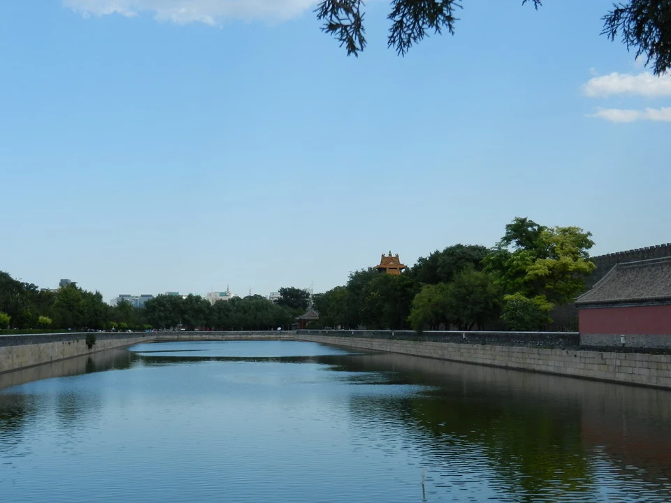 Vista panoramica del fossato della Città Proibita a Pechino con alberi e edifici in lontananza.