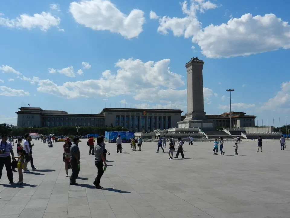 Una veduta ampia della Piazza Tiananmen a Pechino con edifici storici e persone in primo piano.