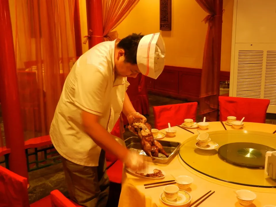 Un uomo in camicia da cuoco prepara cibo a un tavolo in un ristorante cinese.