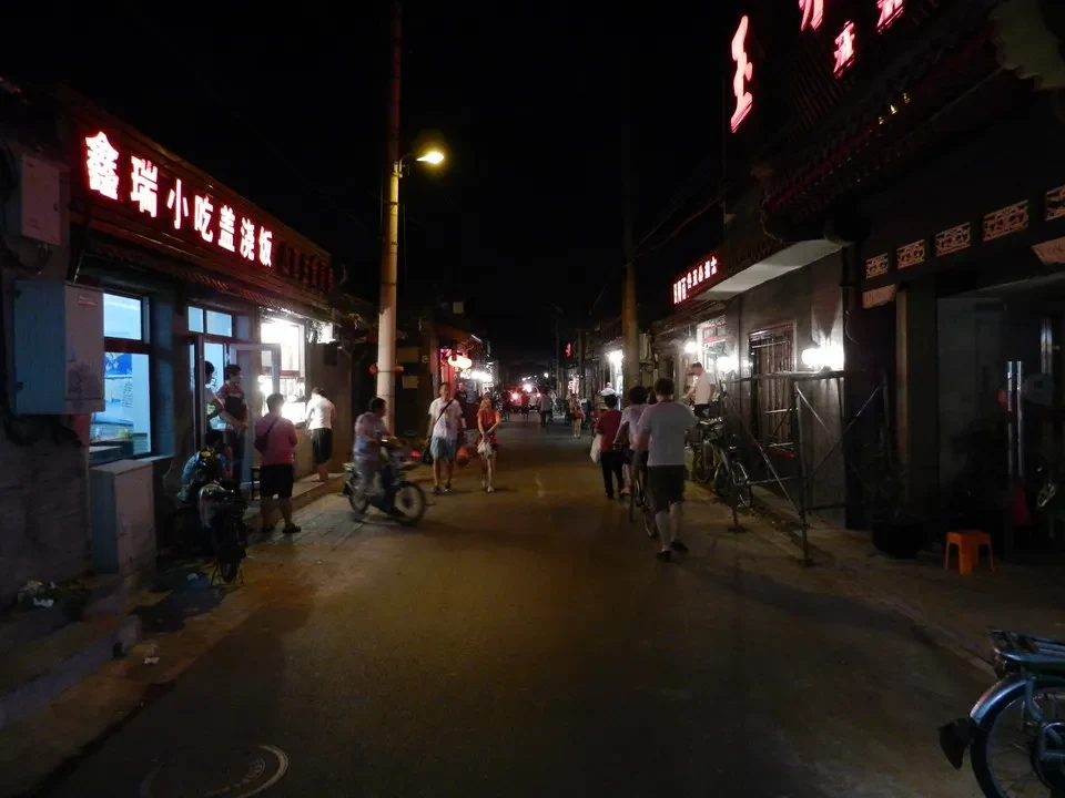 Una strada serale in Cina con negozi illuminati e persone che passeggiano.