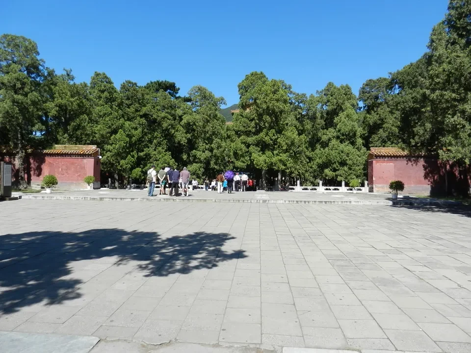 Vista ampia di un cortile pavimentato circondato da alberi e strutture in mattoni rossi.