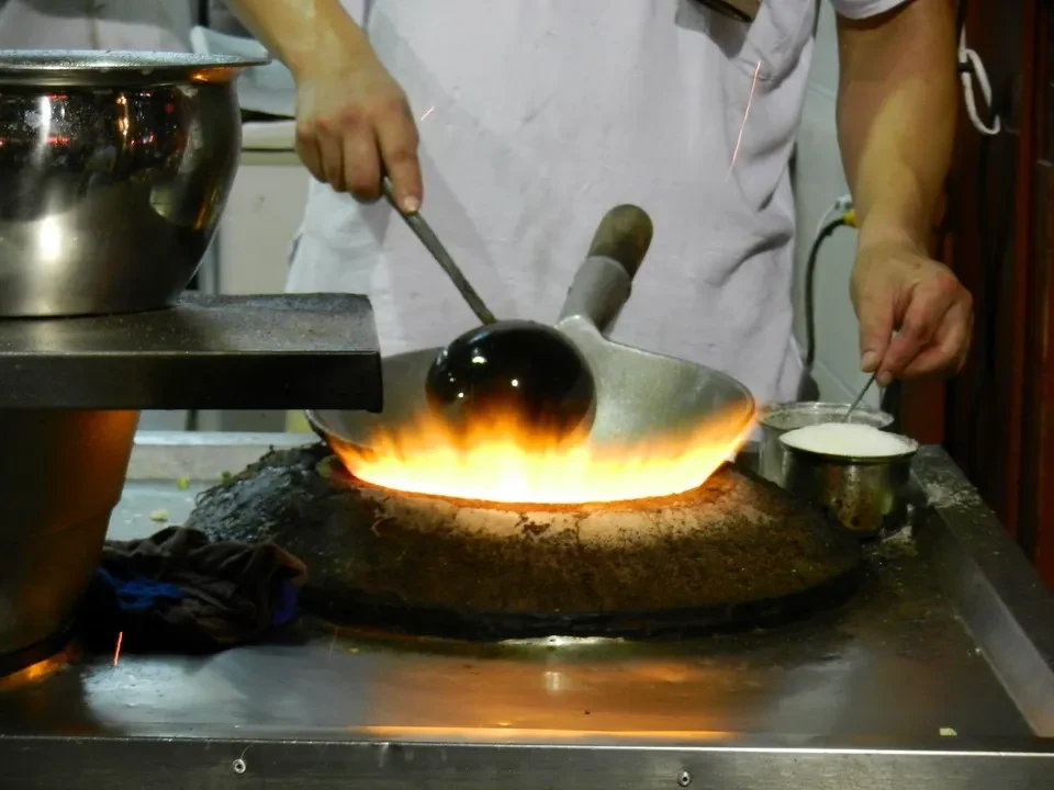 Un cuoco cucina con una padella sopra un fuoco vivo in una cucina cinese.