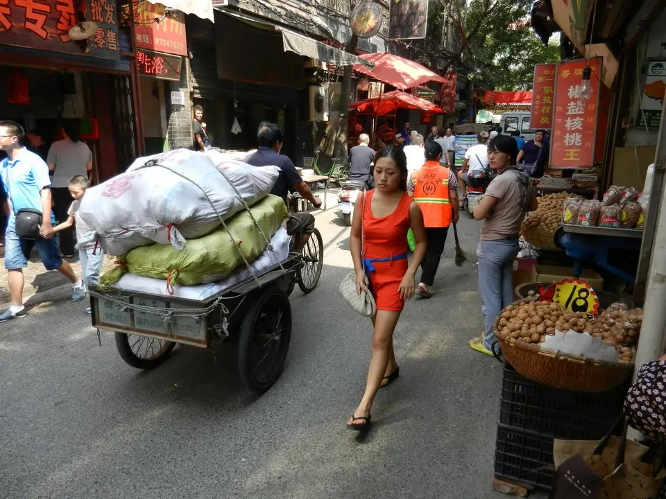 Una donna cammina su una strada commerciale in Cina con merci sulla carrozza.