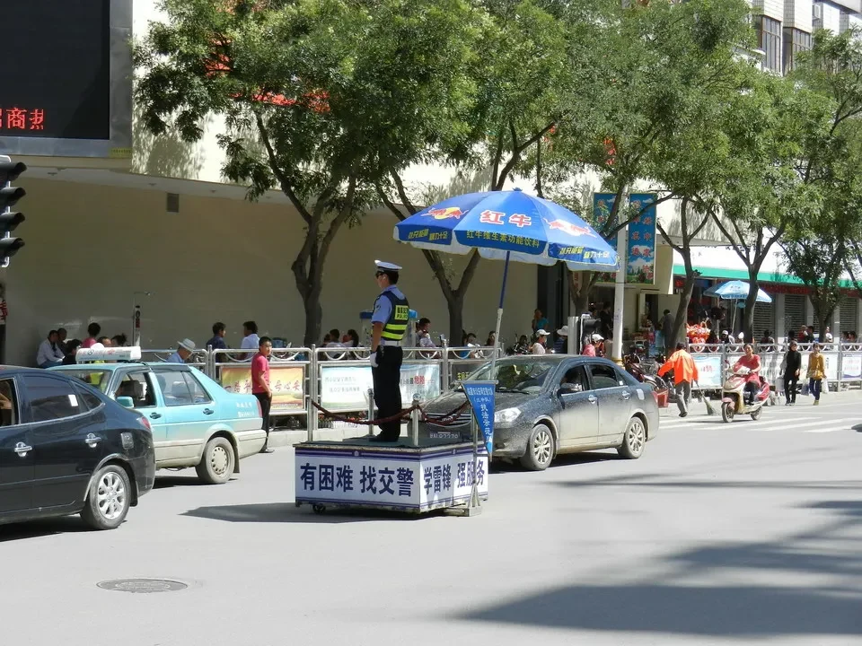 Una scena di strada con veicoli e persone in Cina sotto alberi frondosi.
