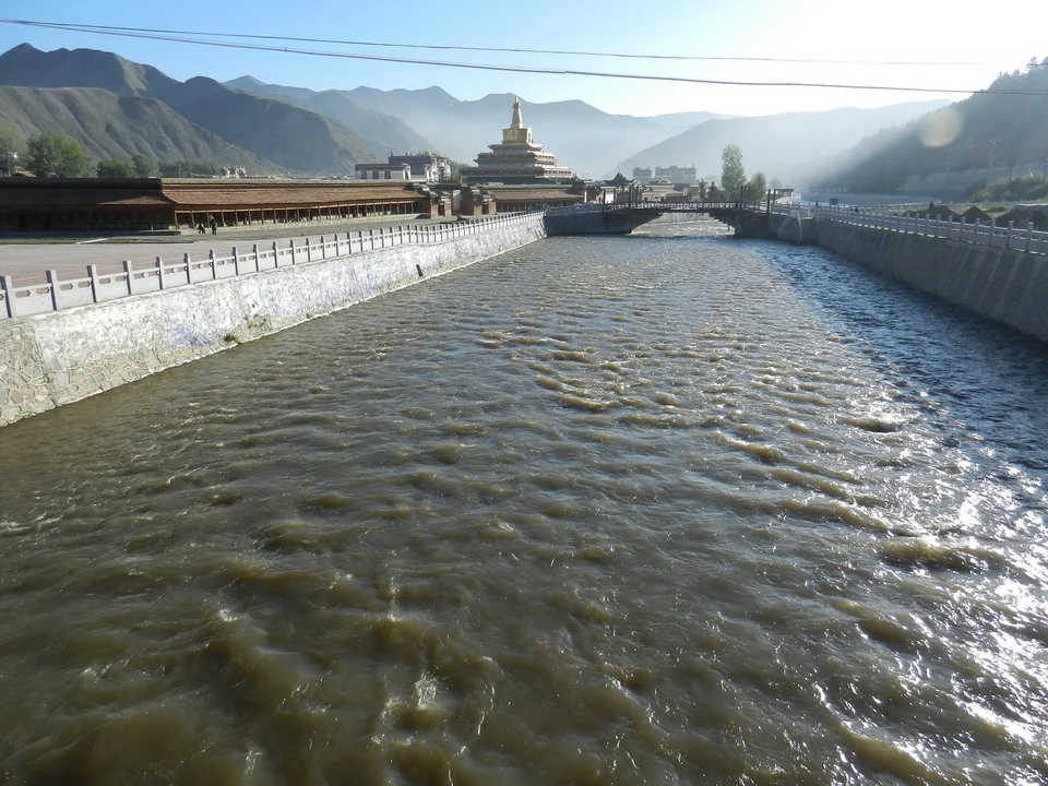 Un ampio fiume scorre attraverso un paesaggio montuoso con strutture lungo le rive.