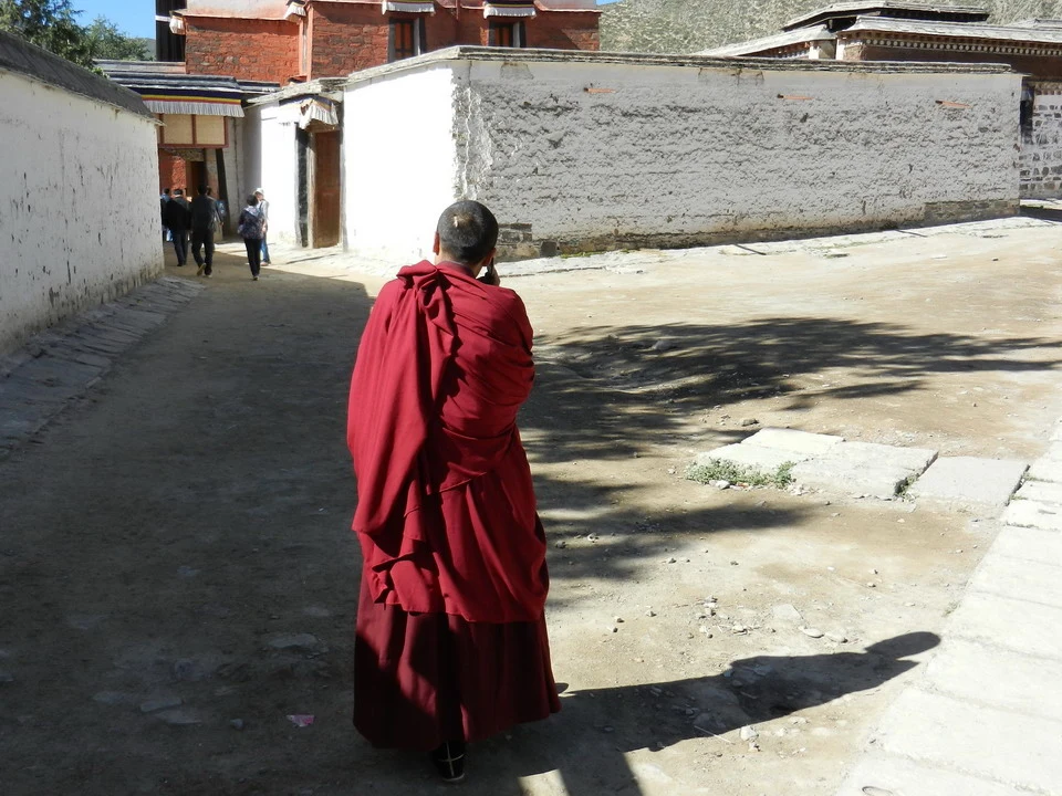Un uomo vestito di rosso cammina lungo una strada interna con mura bianche in Cina.