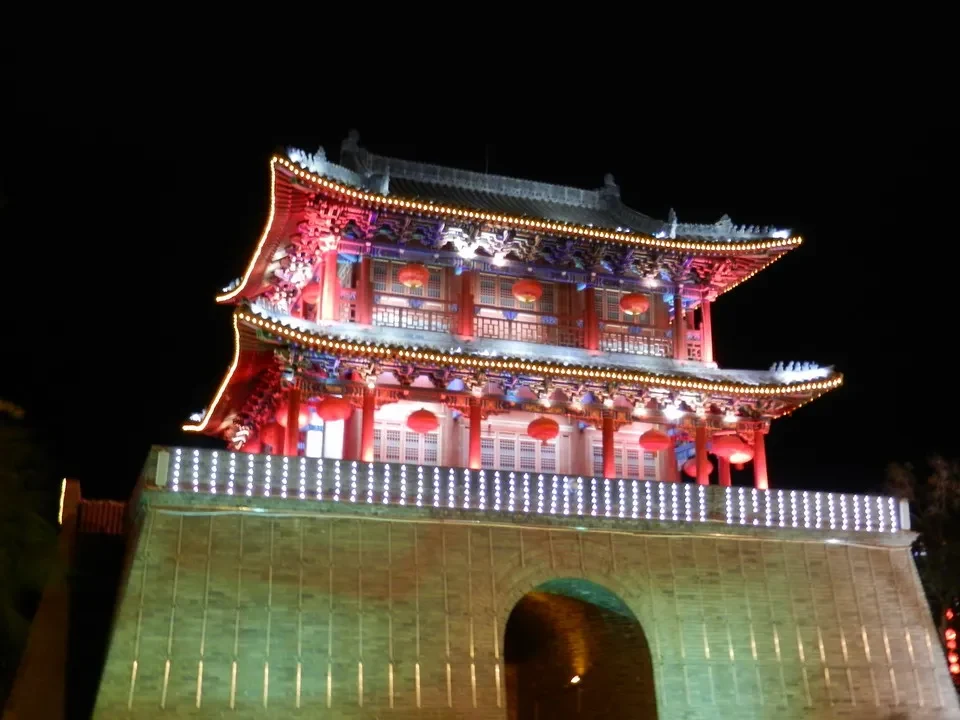 Architettura tradizionale cinese illuminata di notte con decorazioni rosse e dorate.