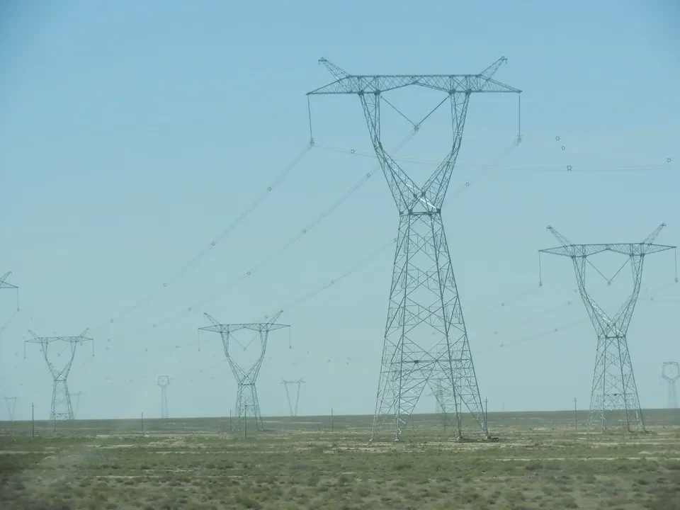 Una linea elettrica a traliccio attraversa un paesaggio aperto sotto un cielo chiaro.